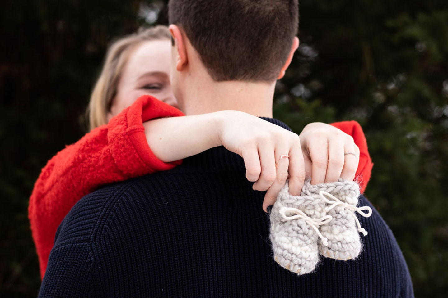 maternity photo with baby shoes over man's shoulder